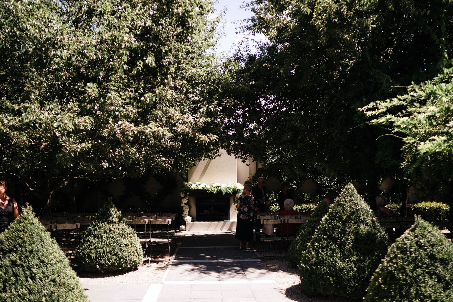 A garden path leads to an elegant white gazebo surrounded by manicured topiary bushes and lush trees.