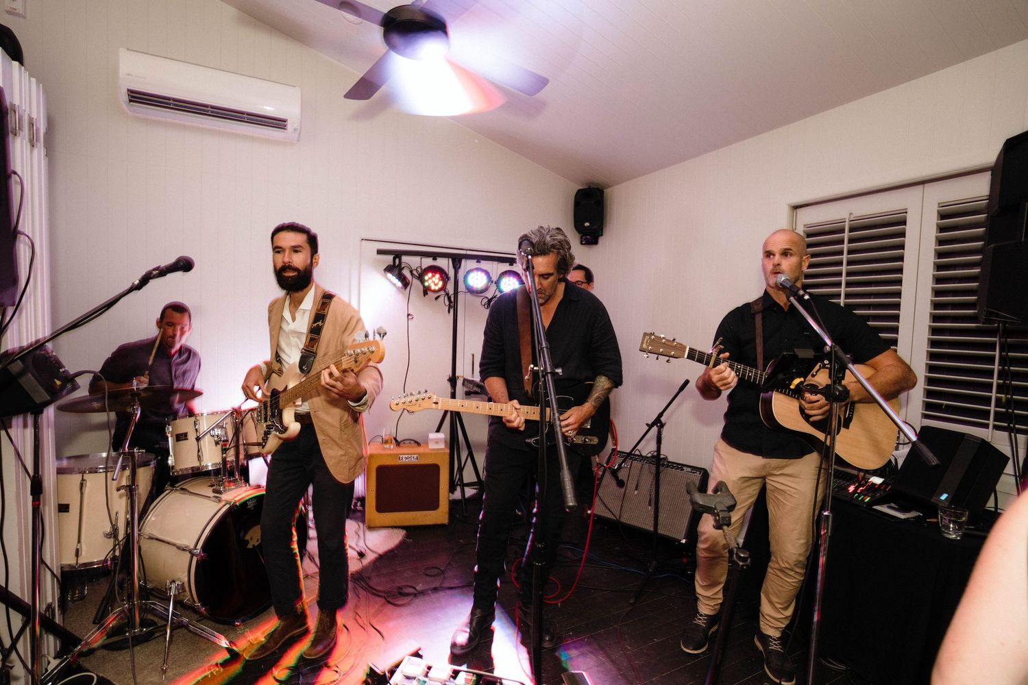 Musicians playing instruments and singing during a live performance in a small indoor space.