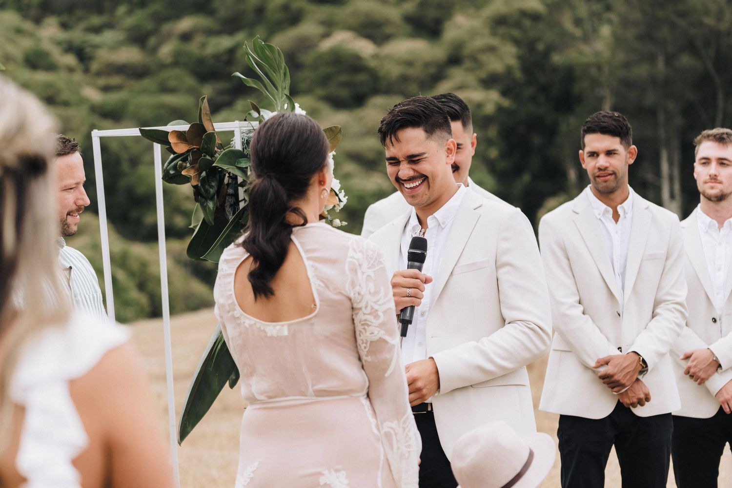 A wedding ceremony taking place outdoors with attendees in white formal attire.