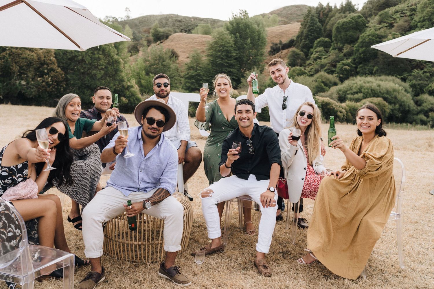 Wedding guests seated in informal outdoor setting with umbrellas and natural scenery.