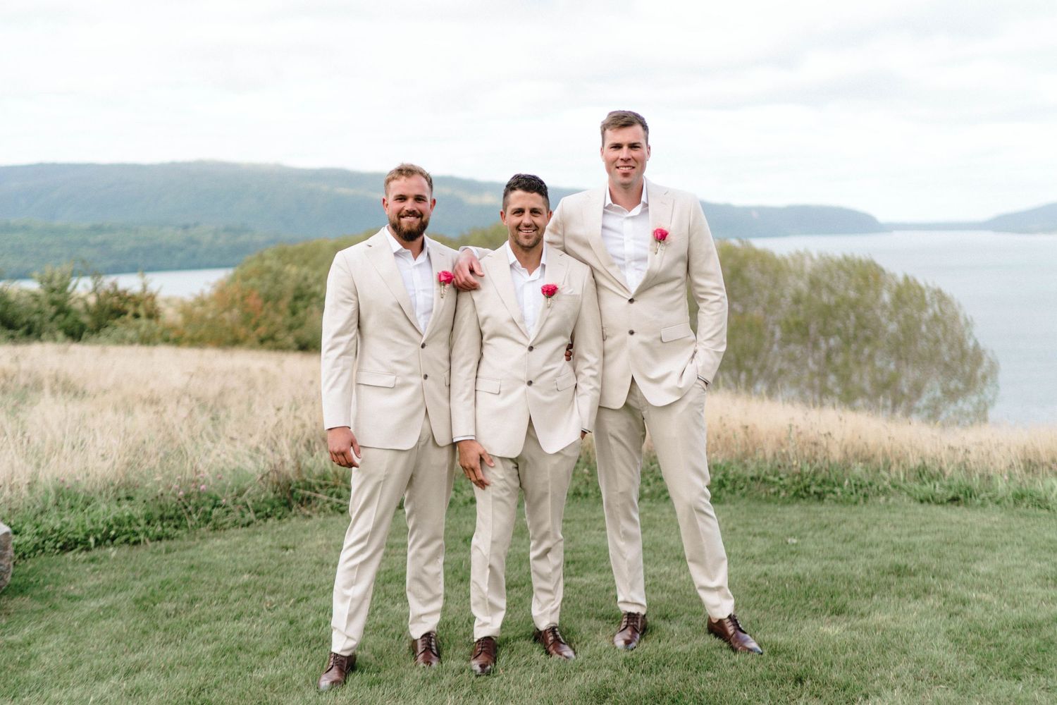 Wedding party in cream colored suits posing on hilltop with water view.