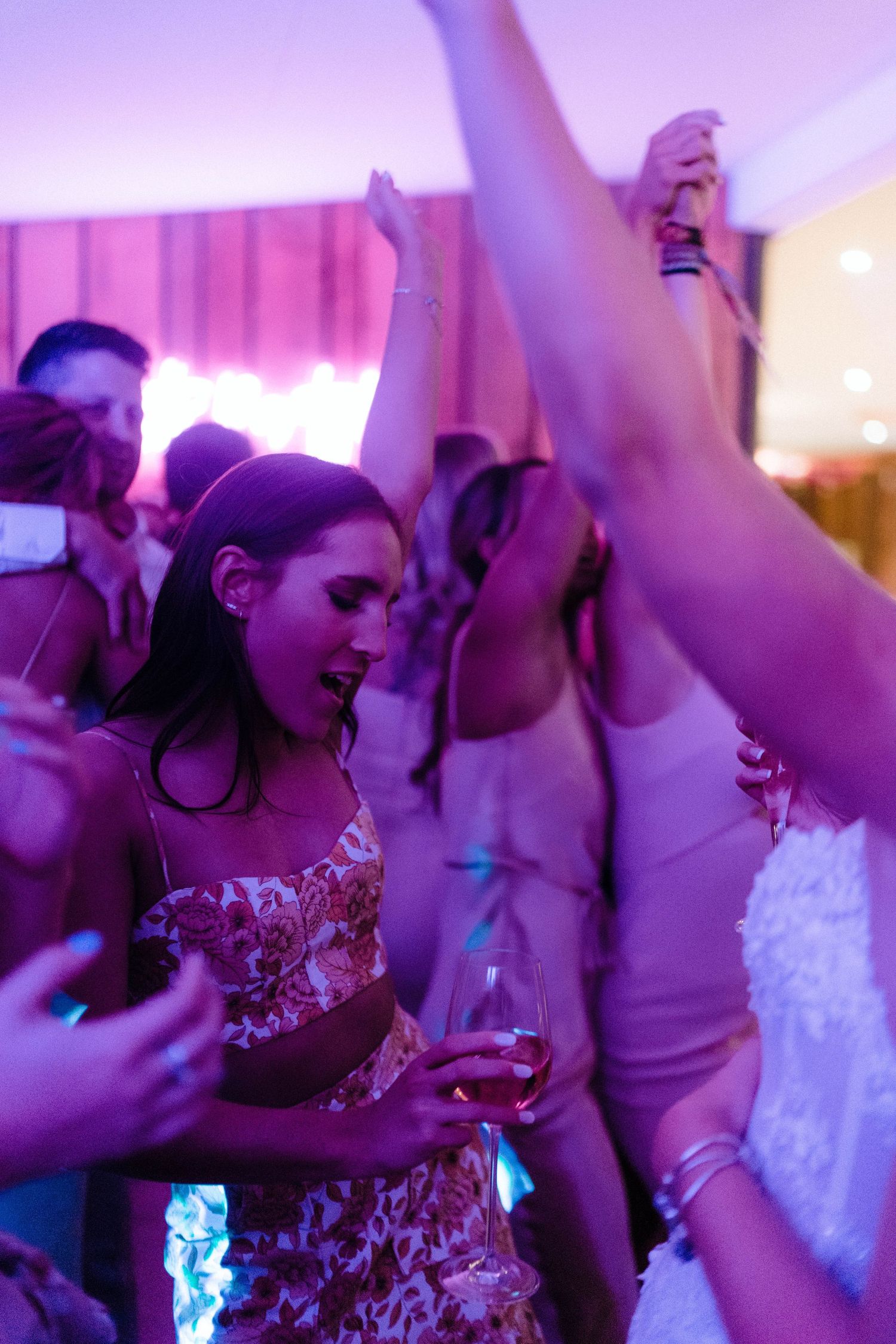 Guests dancing and celebrating at wedding reception bathed in purple lighting.