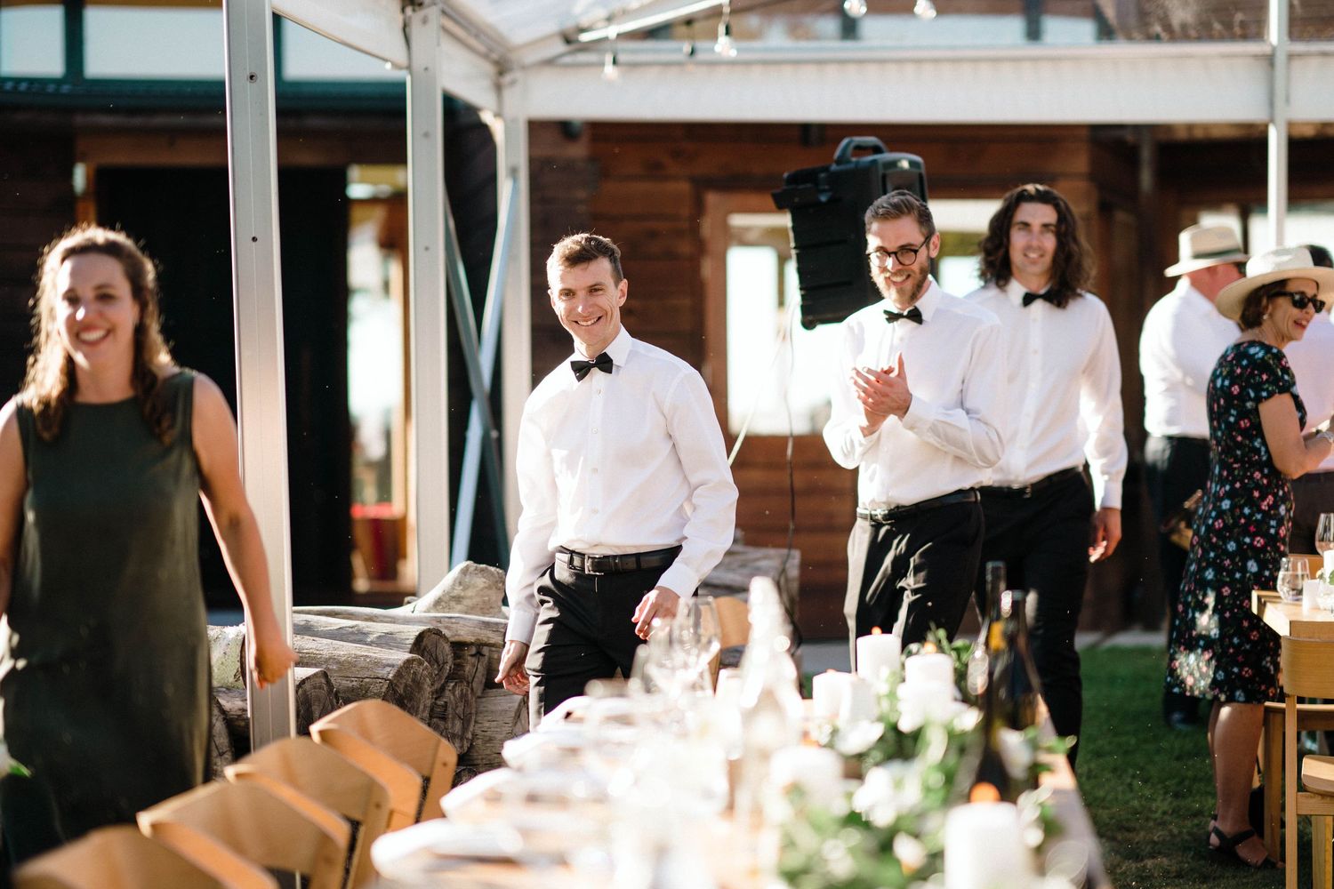 Wedding reception staff preparing elegant table settings under a covered outdoor venue.