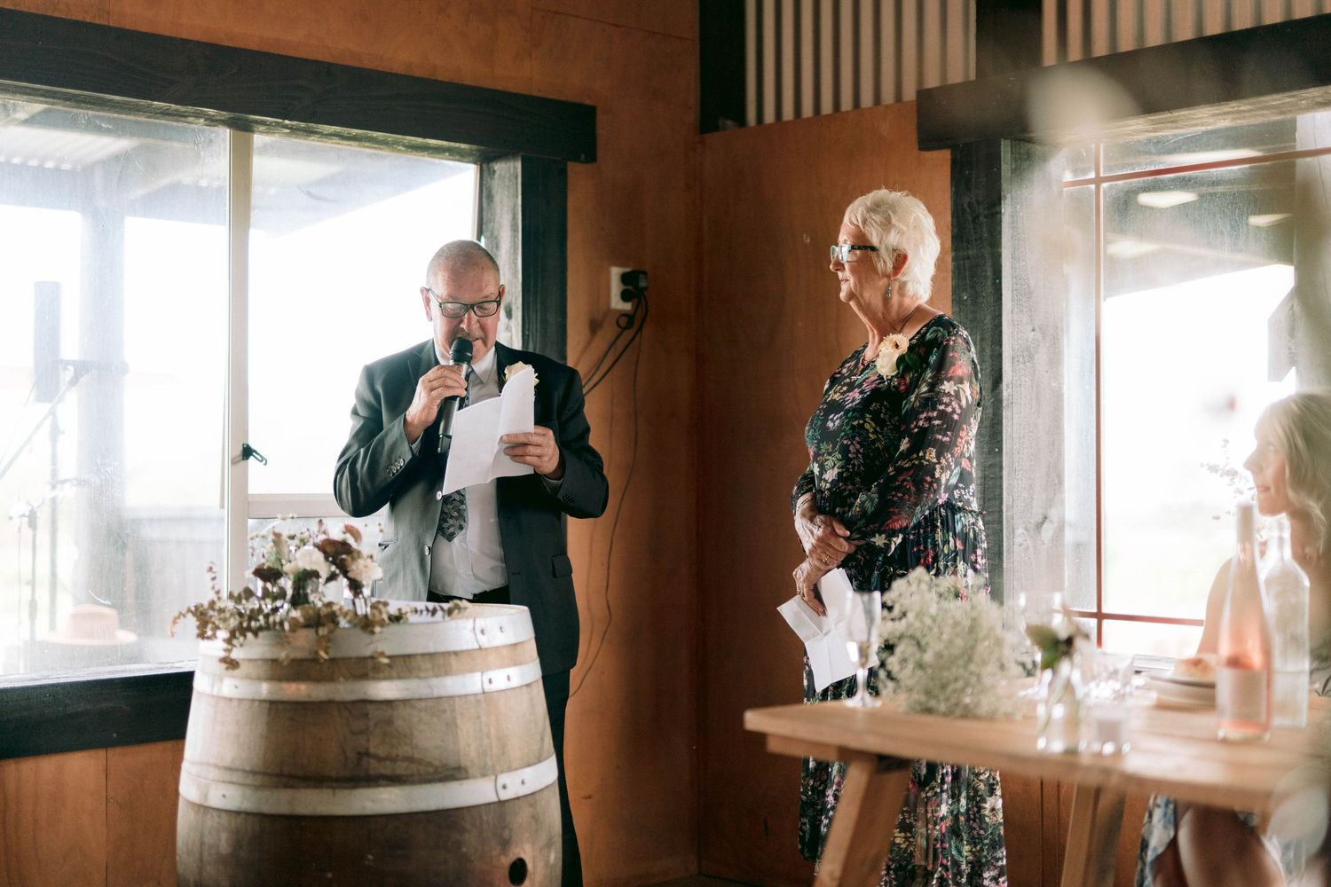 Wedding speeches being delivered near a decorative wine barrel in a rustic venue.
