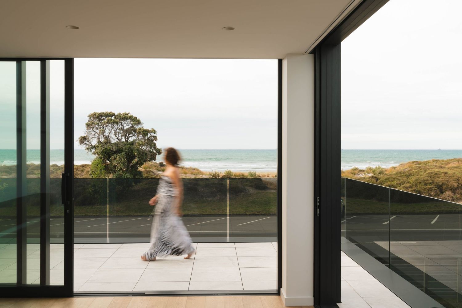 Minimalist interior space with floor-to-ceiling windows overlooking an ocean view and beachfront.