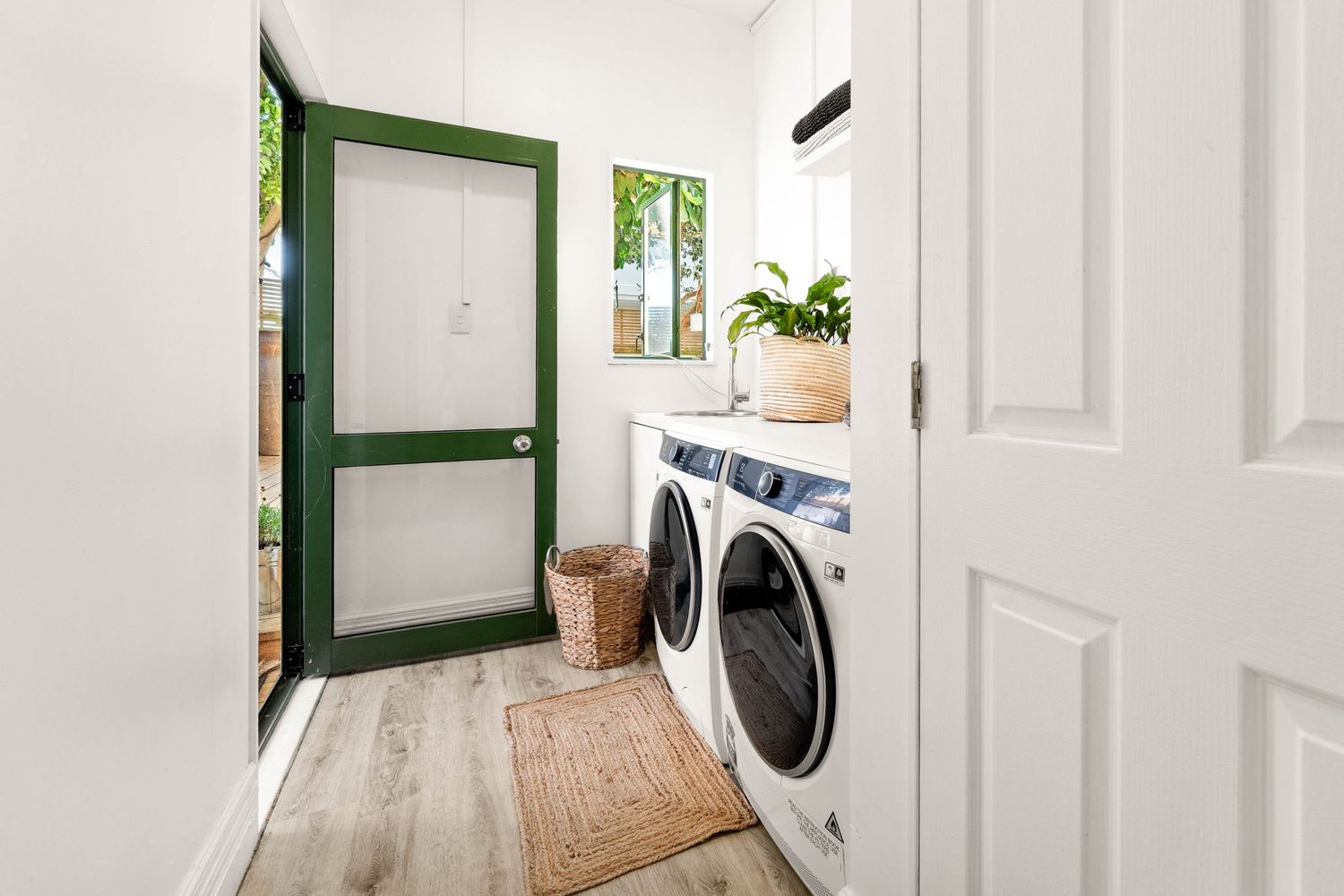 Bright laundry room with green door, modern washer and dryer, and natural decor elements.