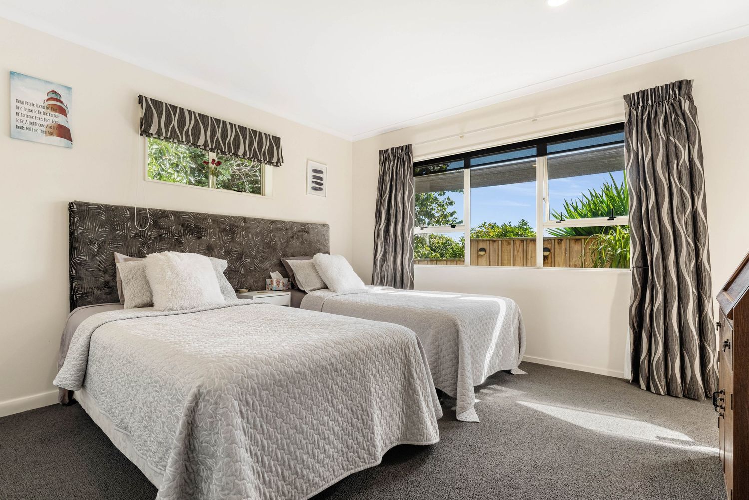 Modern bedroom with two single beds, gray carpet, and zebra-striped curtains in front of a bright window.