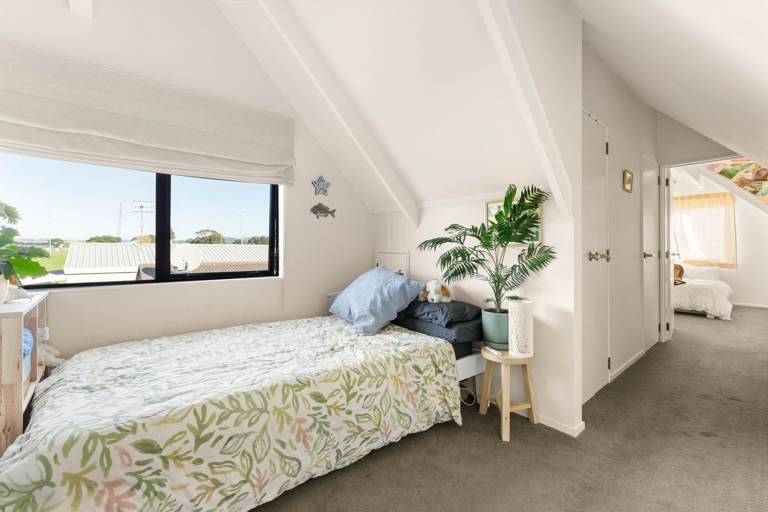 Modern bedroom with floral bedding, houseplants, and large window offering natural light in an attic-style space.