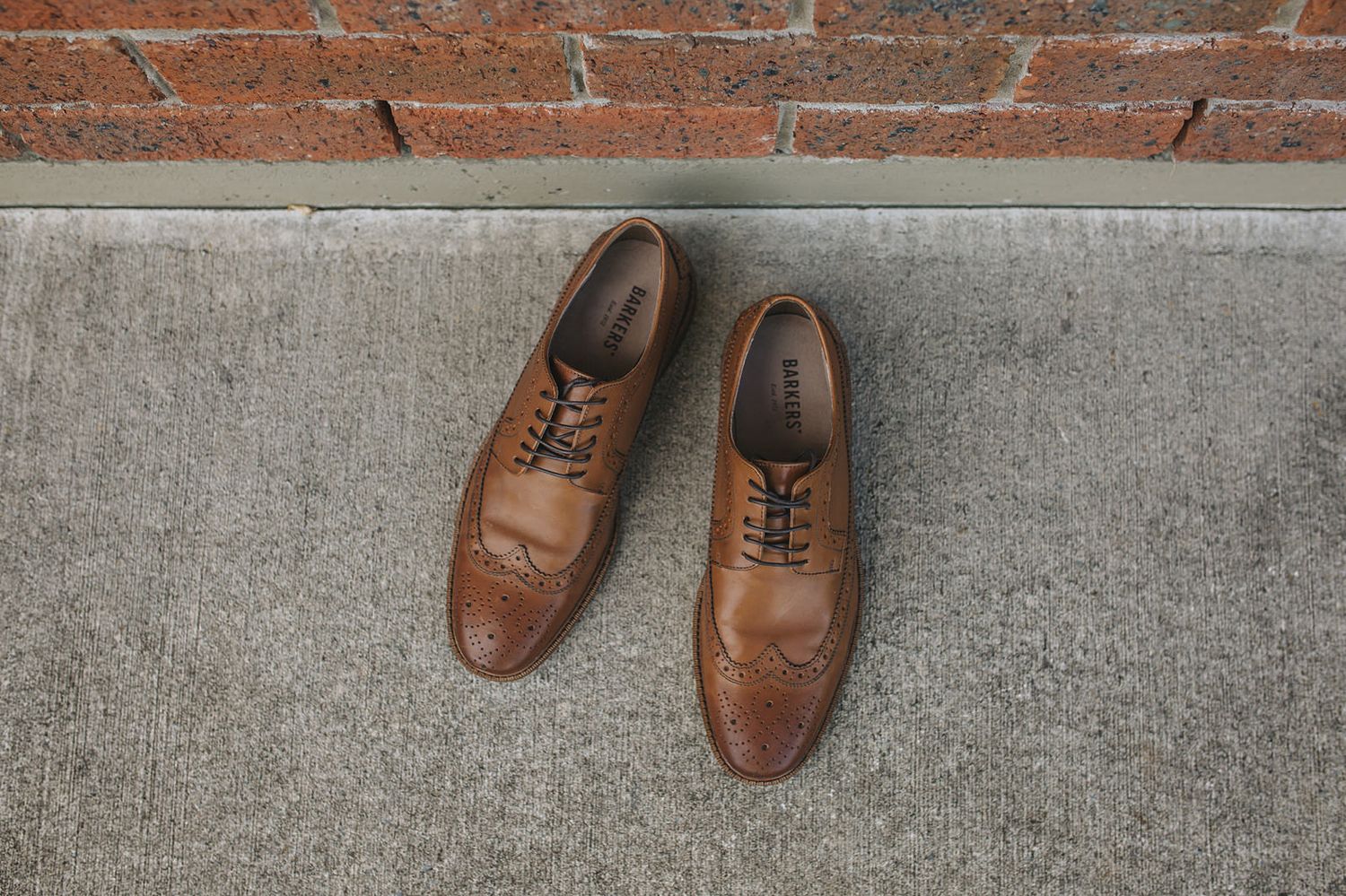 Seven pairs of brown leather oxford dress shoes arranged in a linear progression on a gray concrete surface.