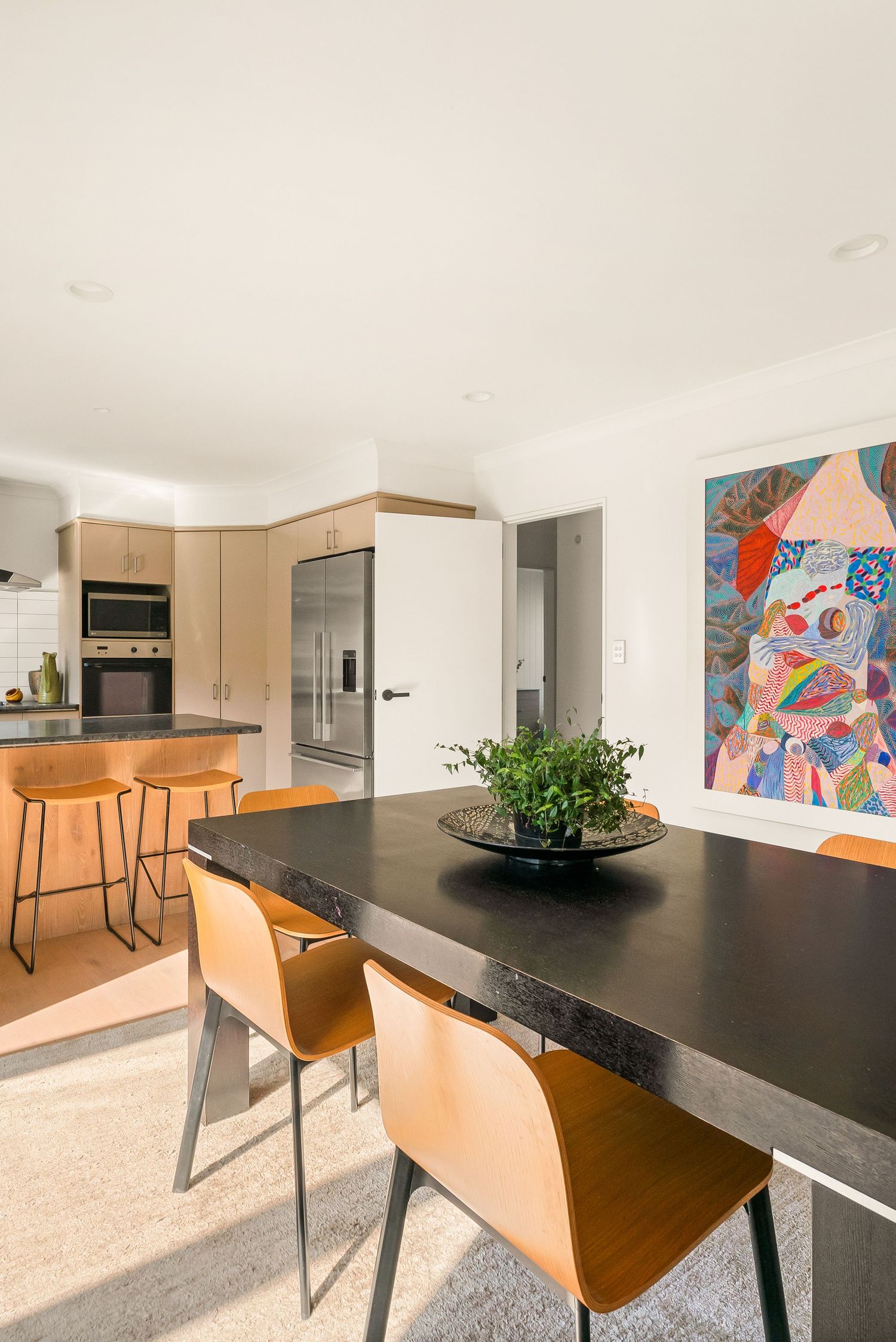 Modern open kitchen and dining area with wooden chairs, black table, and colorful abstract wall art.