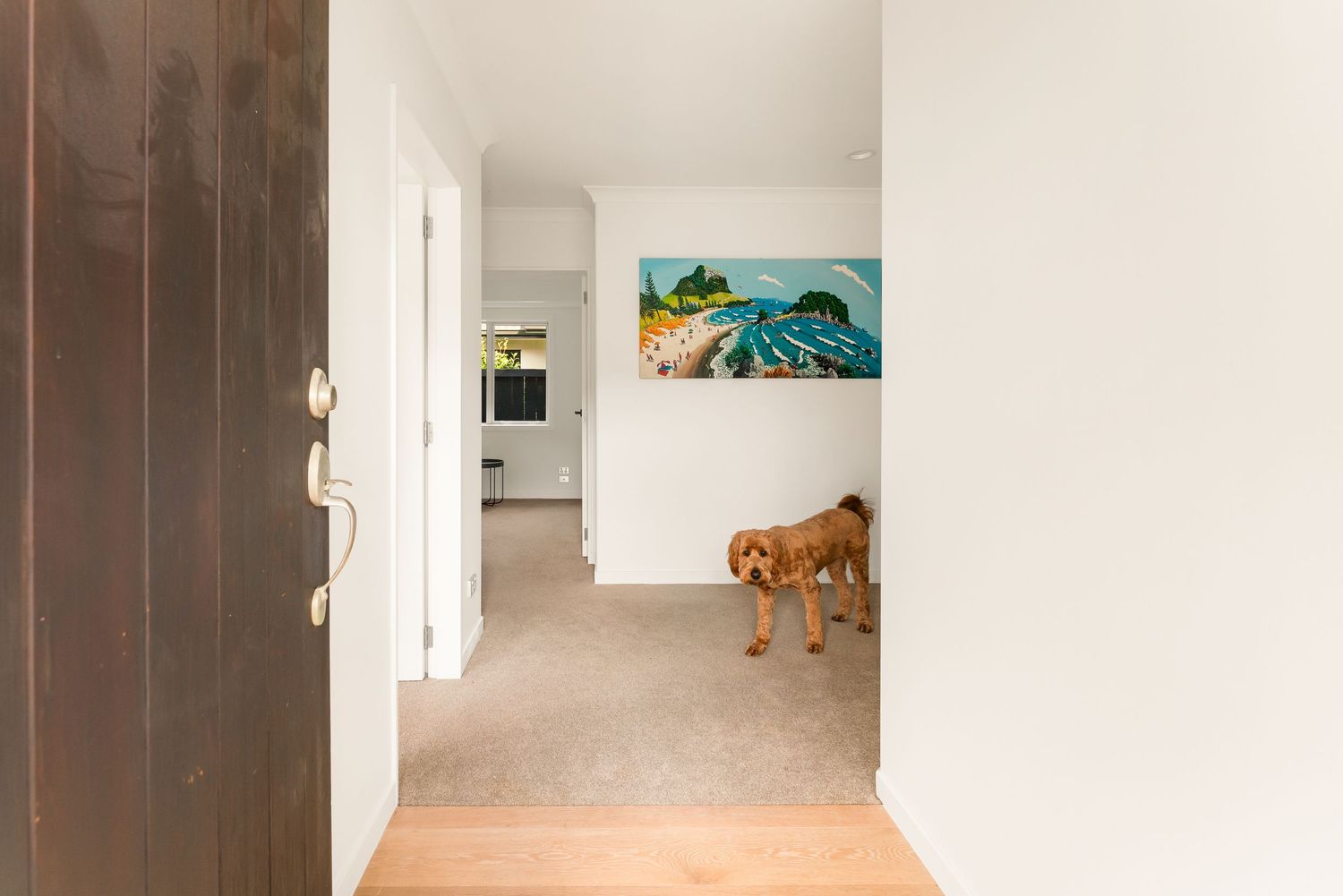 Hallway with hardwood and carpet flooring, featuring vibrant wall art and warm wood door.