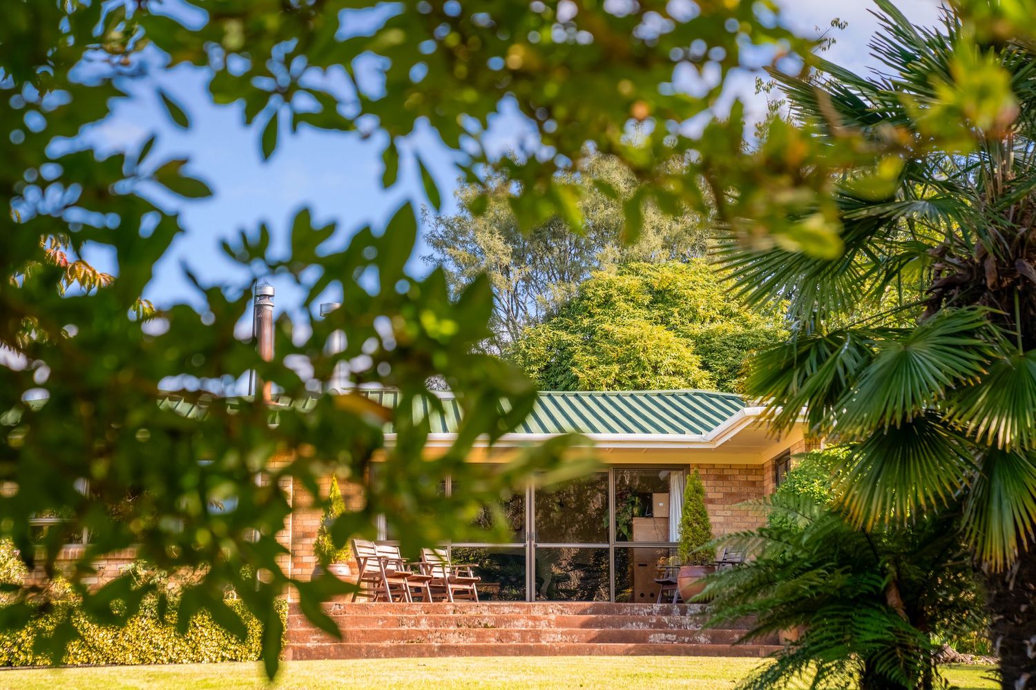 Charming country house with green metal roof viewed through leafy tree branches.