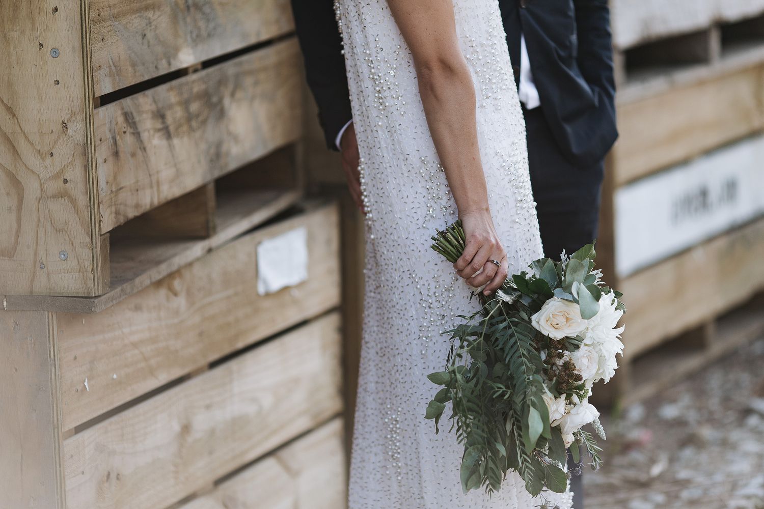 A close-up view of a white dress and a delicate bouquet of white flowers with evergreen sprigs against wooden walls.