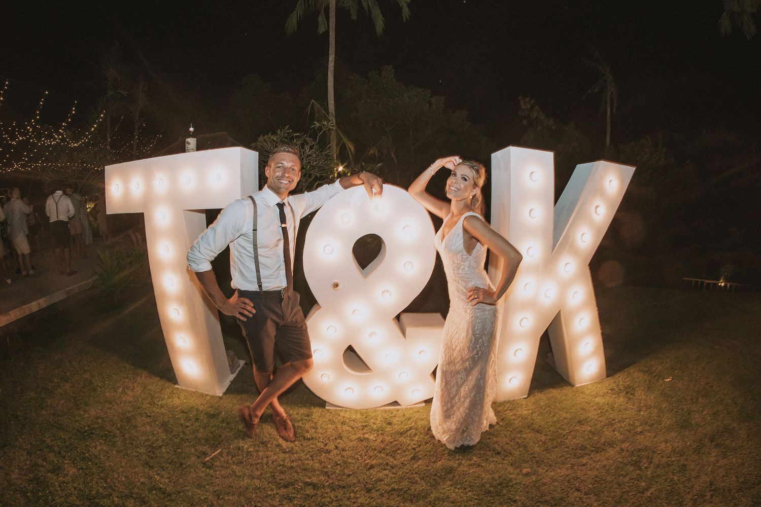 Illuminated marquee letters spelling out initials at night for an outdoor wedding reception.