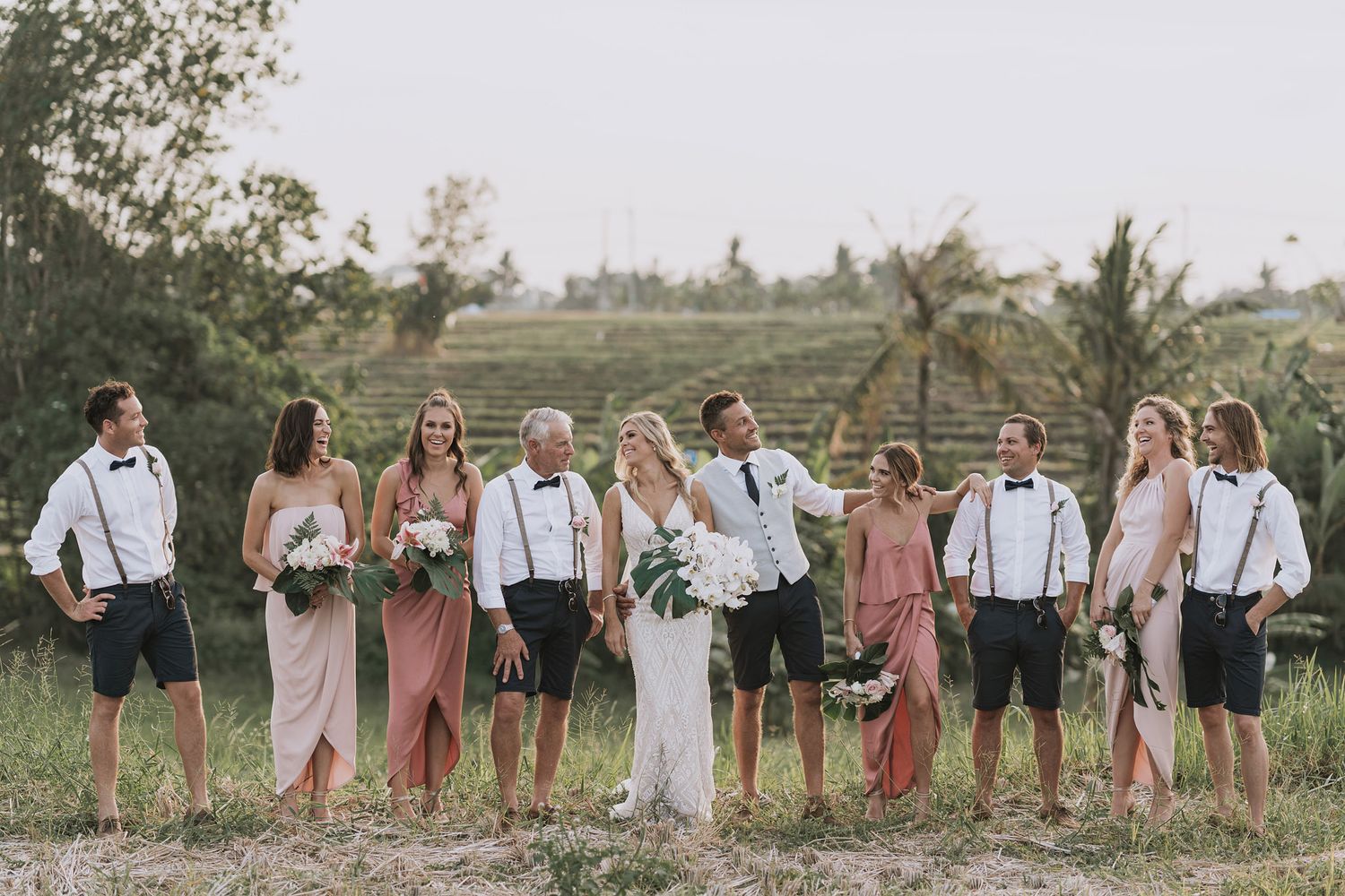 Wedding party poses in an outdoor garden setting with pink bridesmaid dresses and white attire.