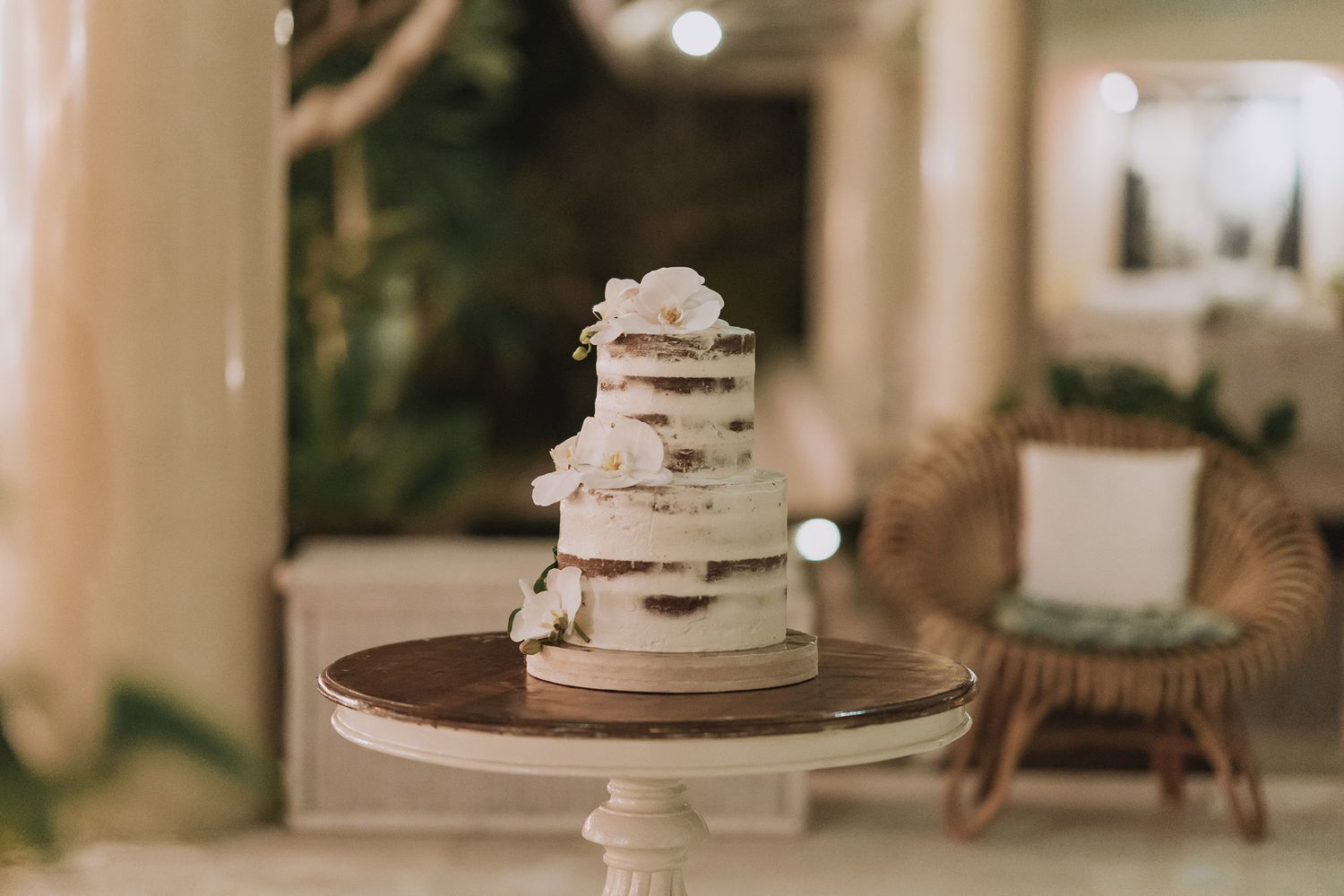 Elegant white semi-naked wedding cake displayed on a pedestal stand with rustic styling.