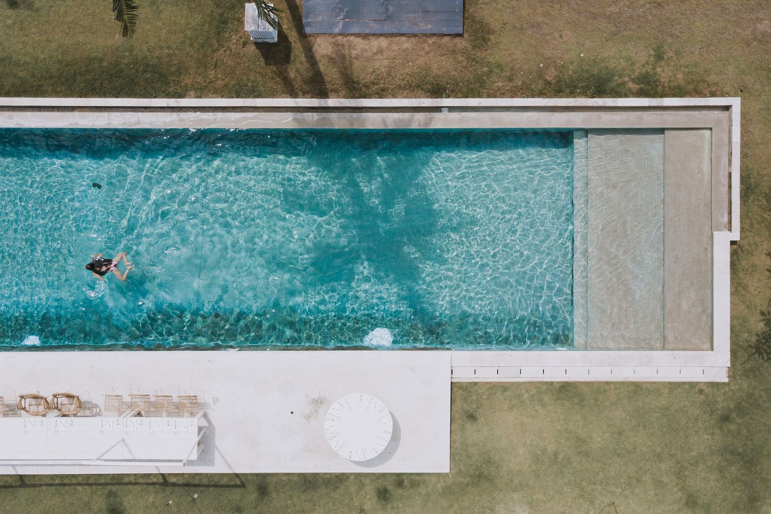 Aerial view of a long rectangular swimming pool with a person swimming in turquoise water.