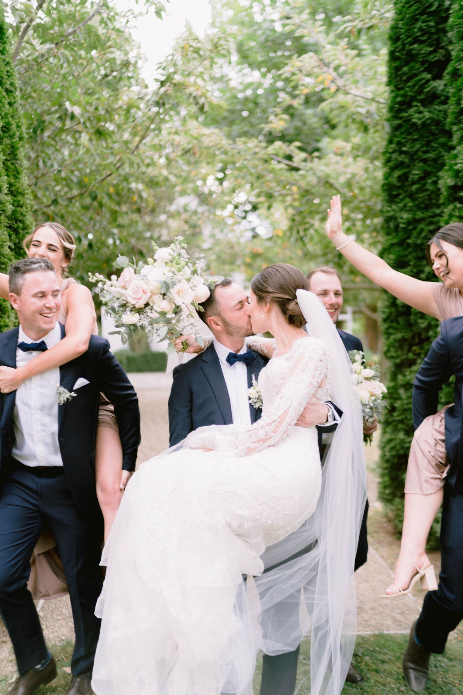 Wedding party celebrates with joy and laughter in a garden setting as newlyweds share romantic moment.