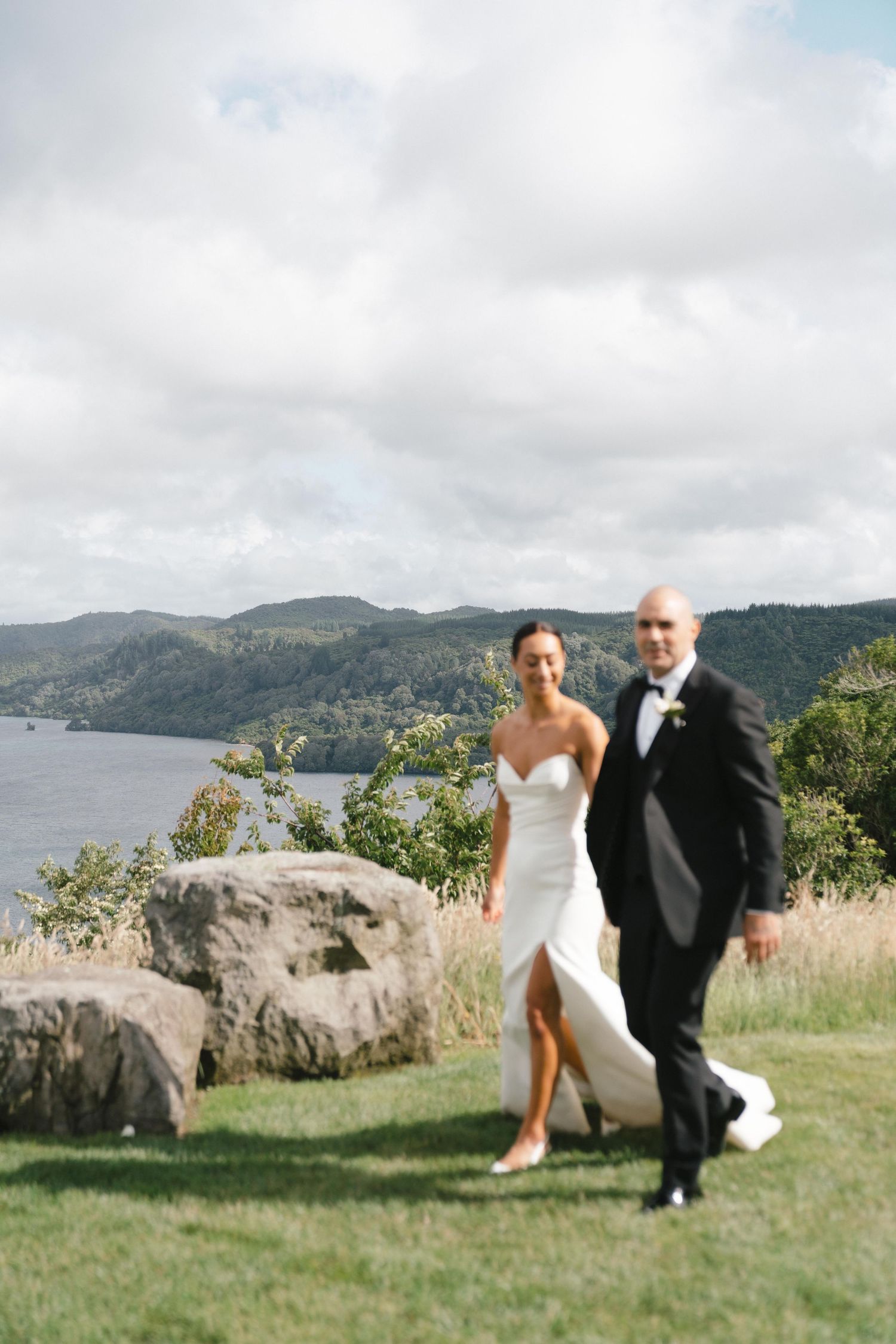 Wedding couple walks along scenic coastal cliff path with ocean views in background.