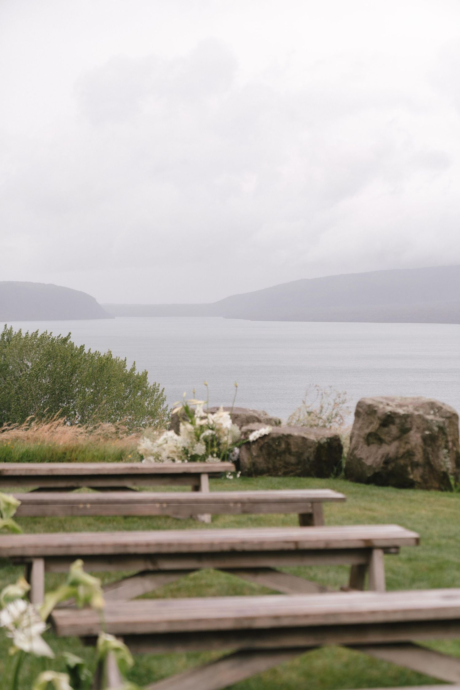 Wooden picnic tables arranged on a grassy hillside overlooking a misty lake.