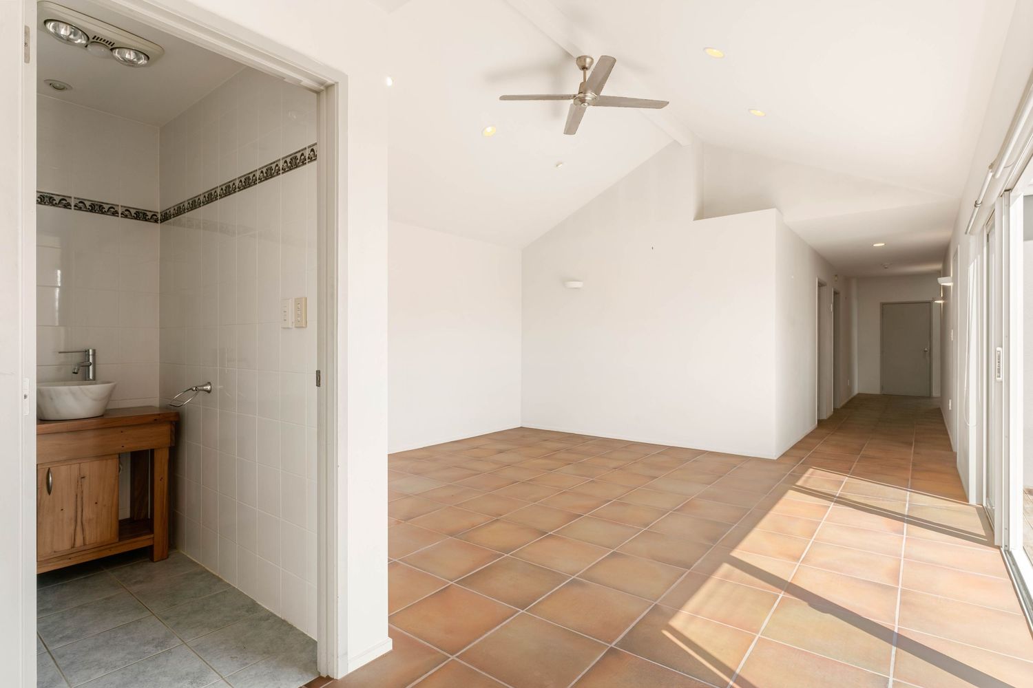 Bright hallway with terracotta flooring, white walls, and a bathroom vanity visible in the corner.