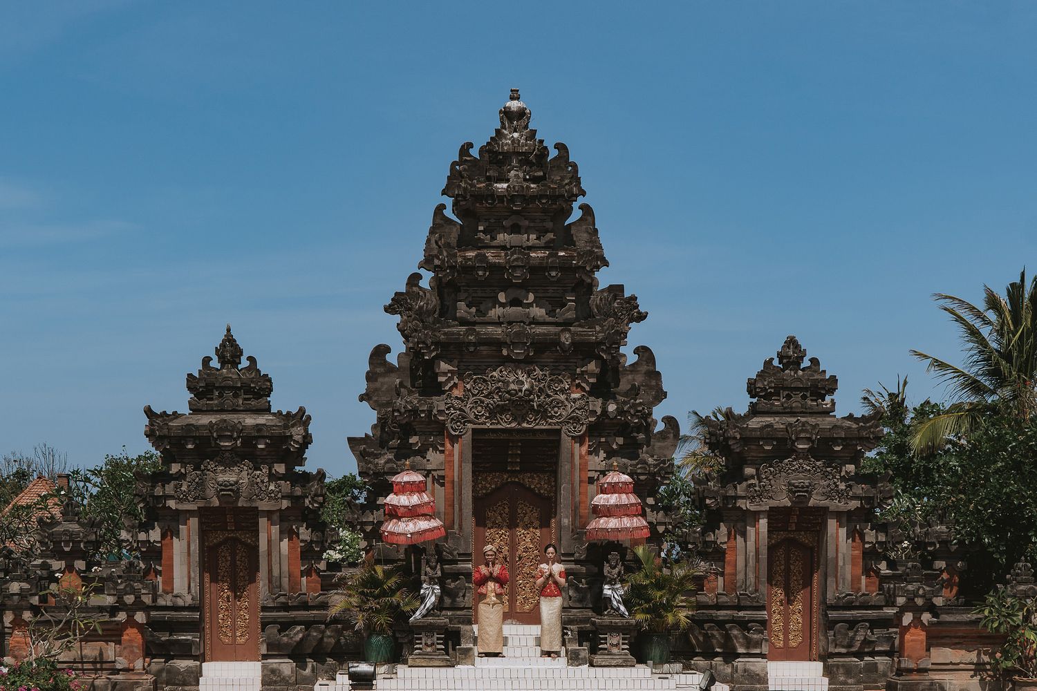 Traditional Balinese temple gates and architecture with ornate stone carvings against blue sky in tropical setting.