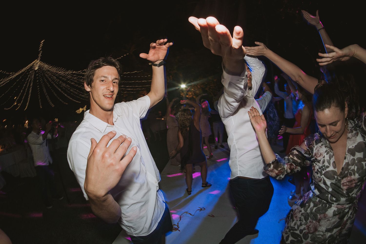Energetic dance floor scene with white-clad guests at nighttime wedding reception.