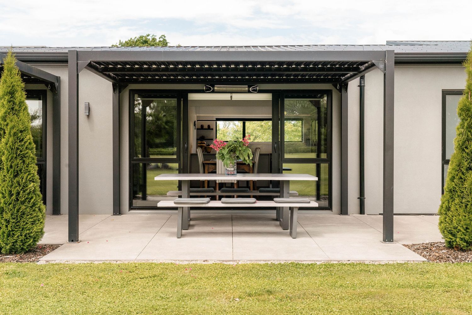 Modern luxury home exterior features expansive glass walls and covered patio overlooking landscaped grounds.
