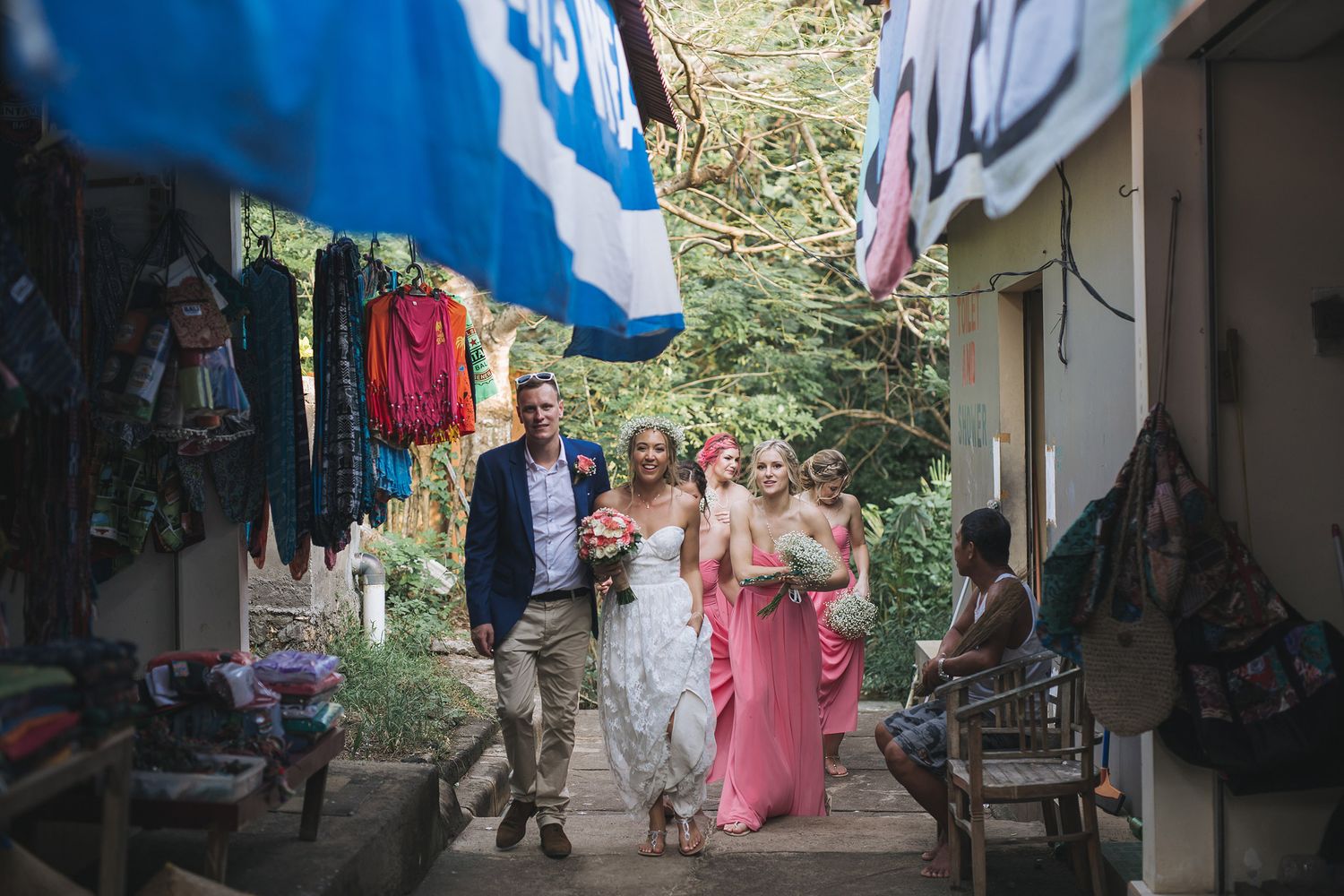 Wedding party walks along a sunny outdoor pathway decorated with flags.