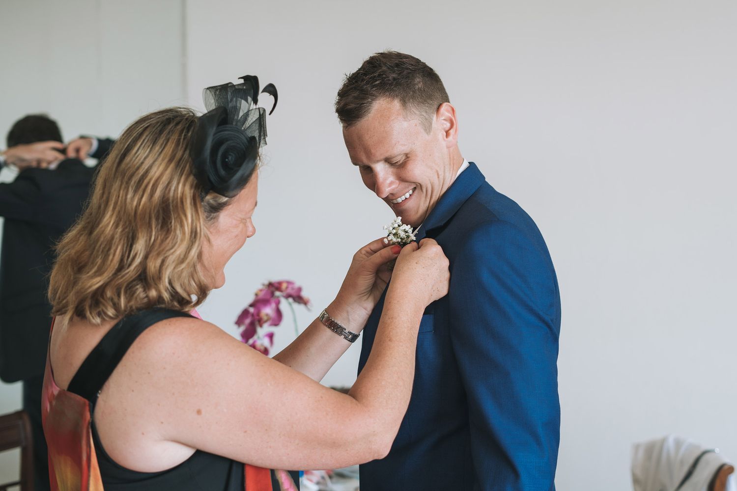 Someone adjusts a boutonniere on a navy blue suit during wedding preparations.
