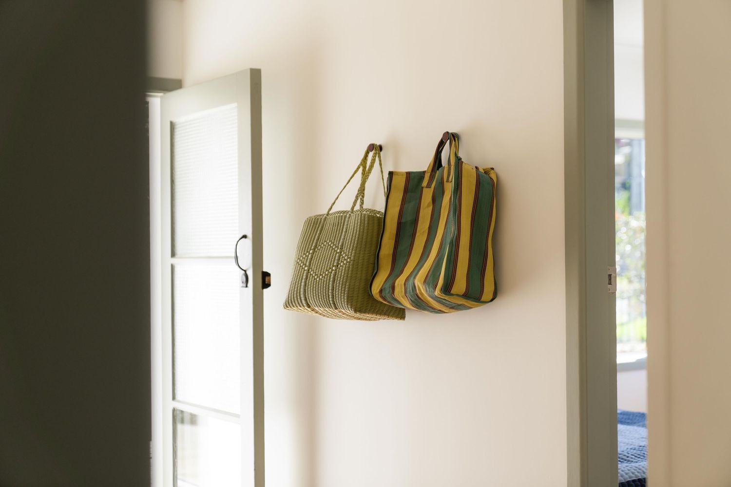 White interior hallway with coat hooks mounted on wall and various bags hanging neatly in a row.