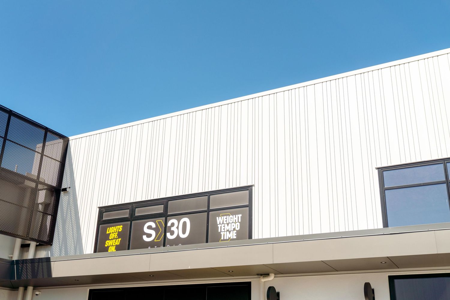 Modern white building exterior with black S30 sign and yellow postal logo on wall against blue sky.