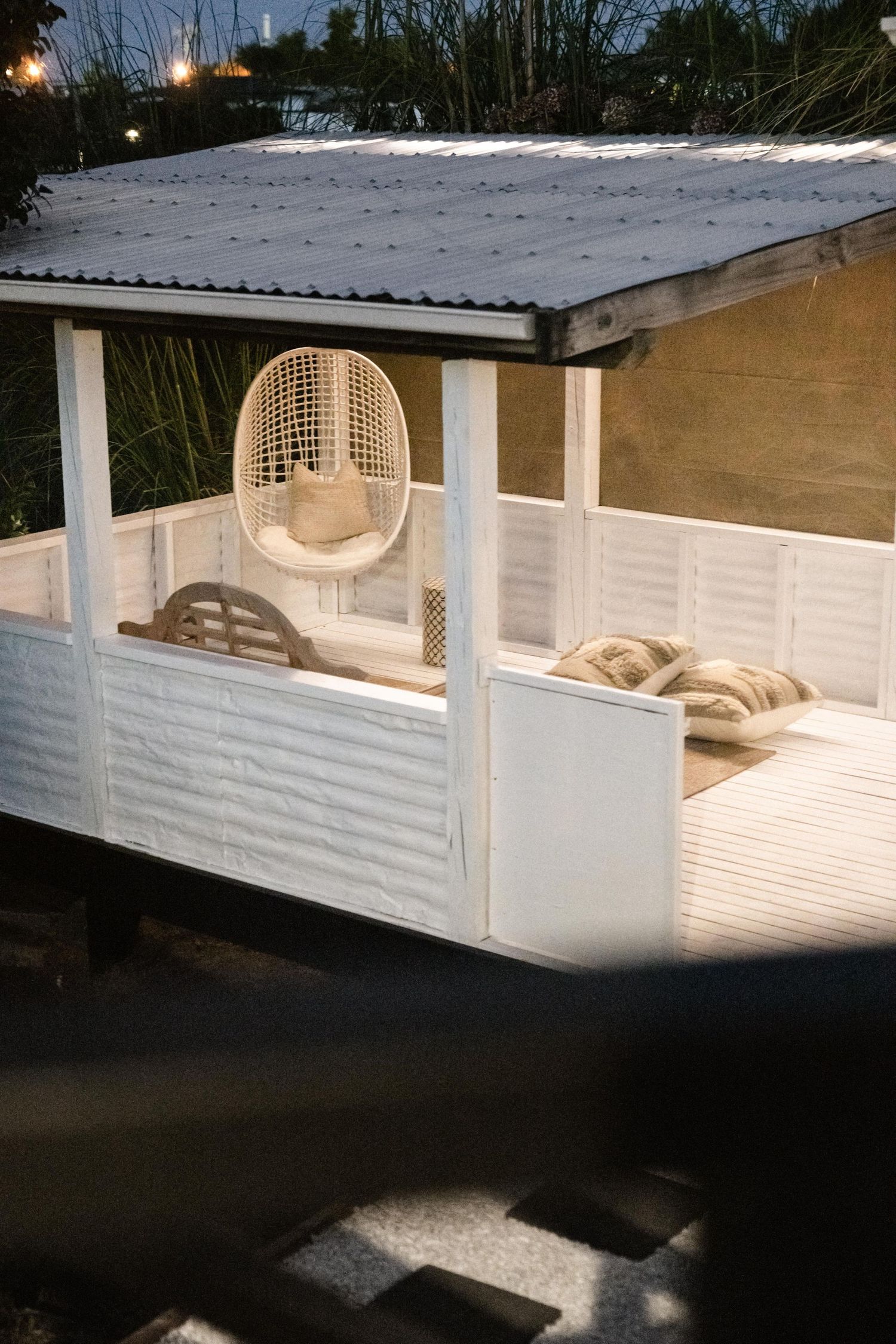 White covered patio with hanging egg chair and cushioned seating under illuminated roof.