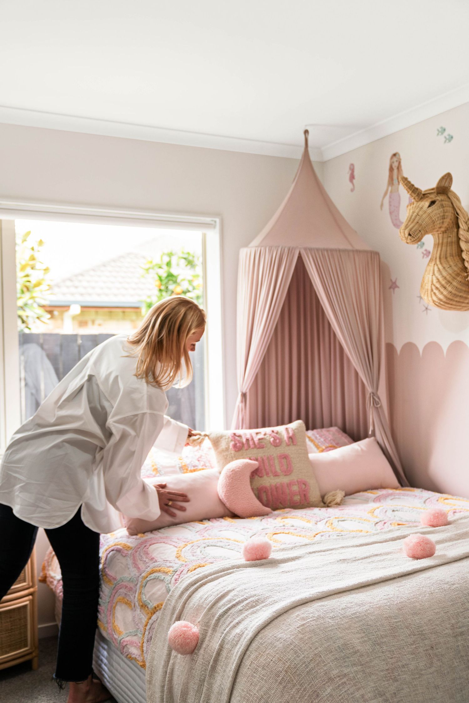 A cozy children's bedroom with pink canopy, floral bedding, and gold wall decor in natural lighting.