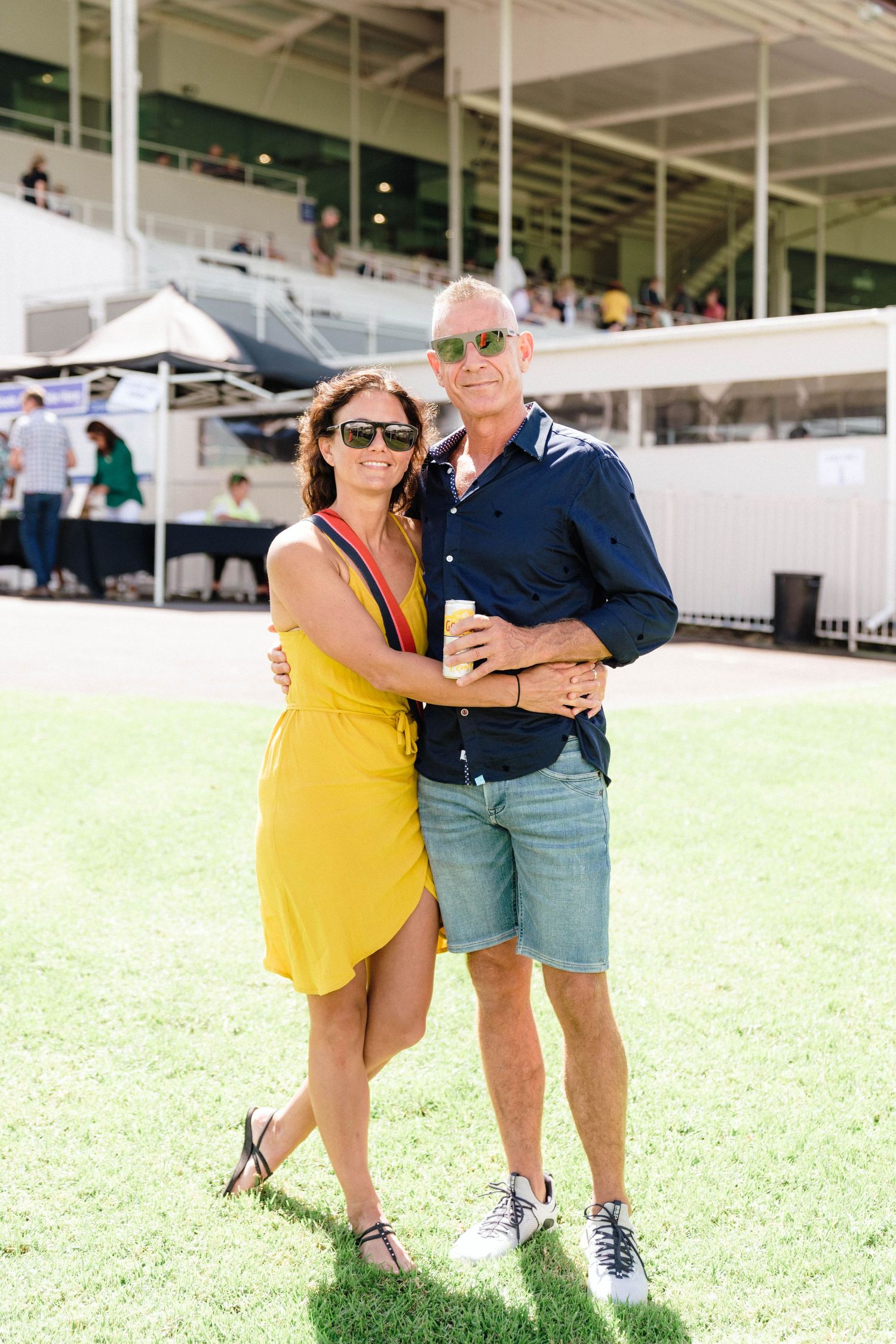 A couple takes selfie photos together at an outdoor venue wearing casual summer attire.