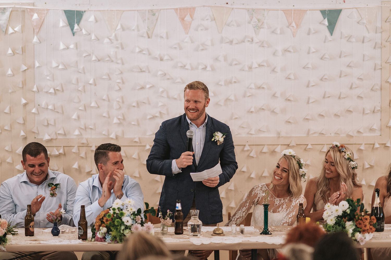 Someone delivers a speech at a wedding reception decorated with bunting and floral arrangements.