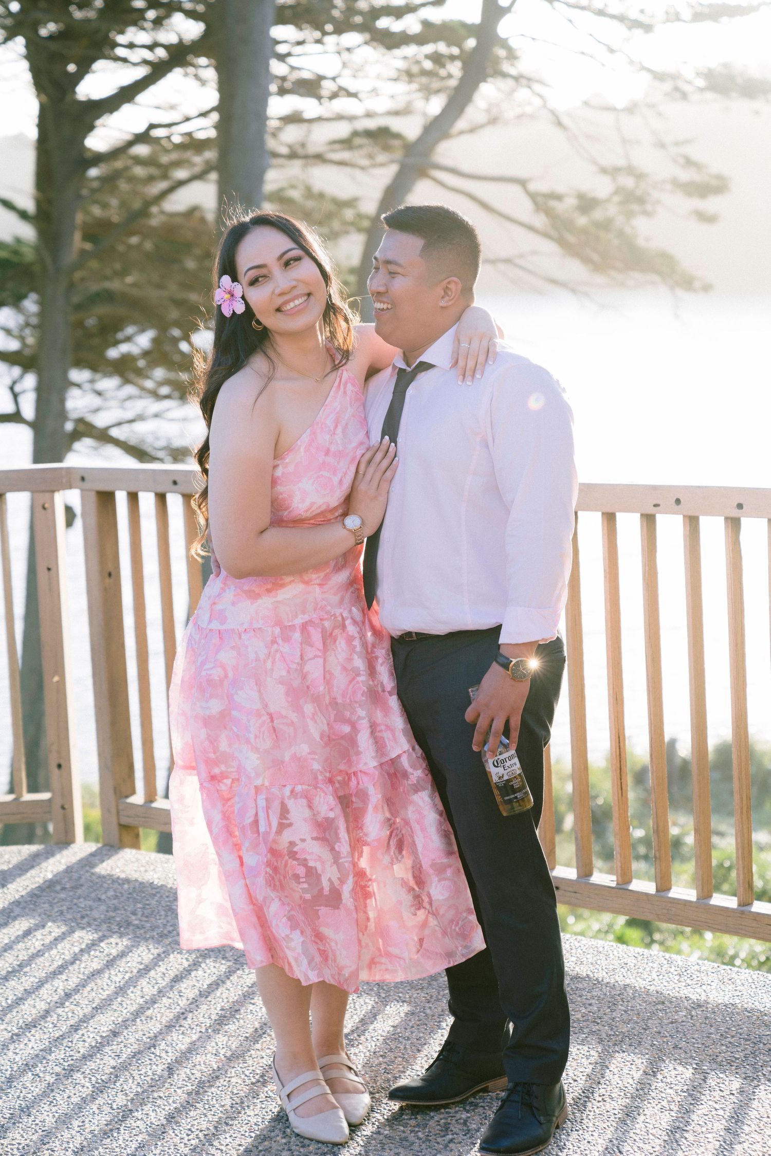 A couple shares a romantic moment on a wooden deck overlooking a misty coastal landscape.