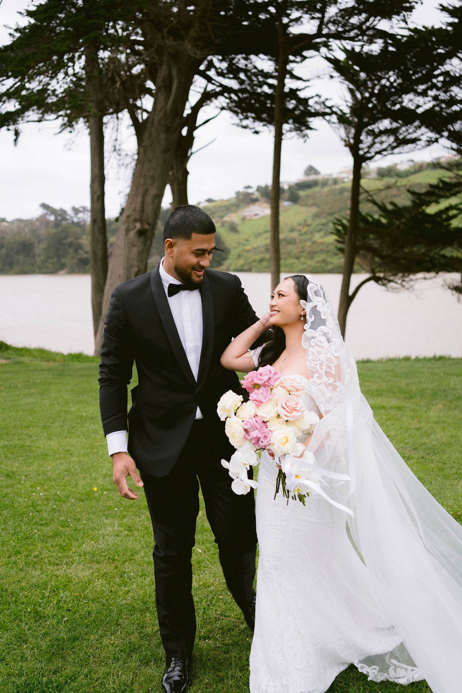 A joyful outdoor wedding moment with a beautiful water view and cypress trees in the background.