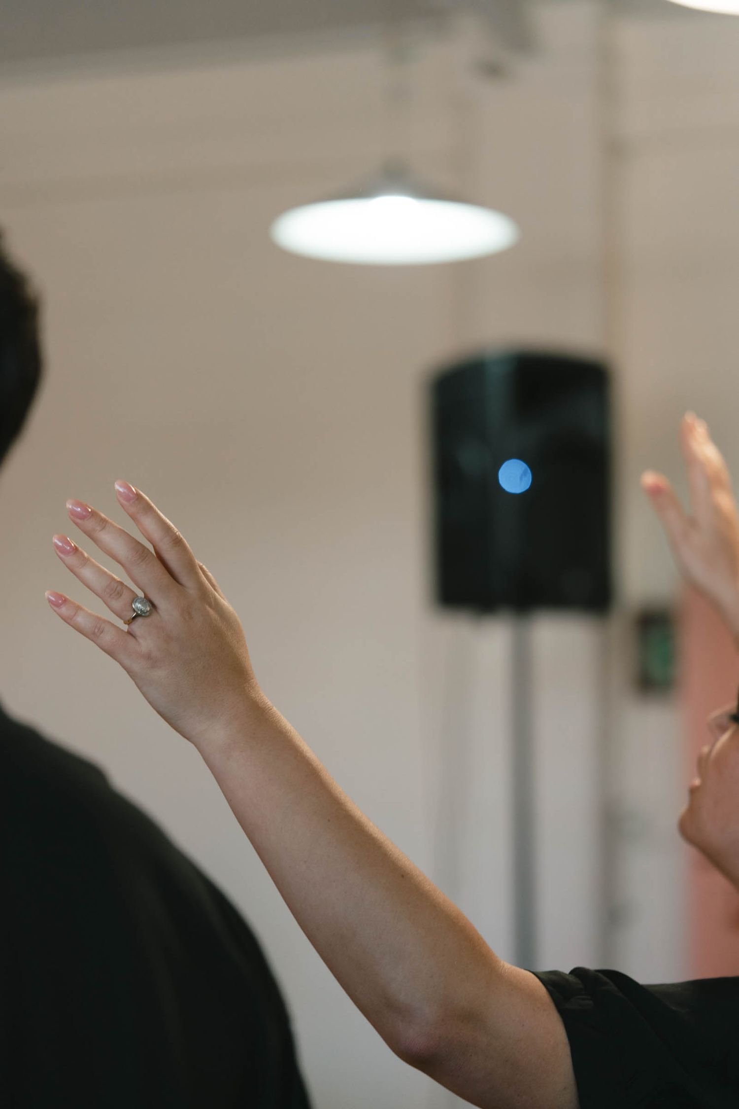 Raised hands during worship with ceiling lights and speakers visible in the background.