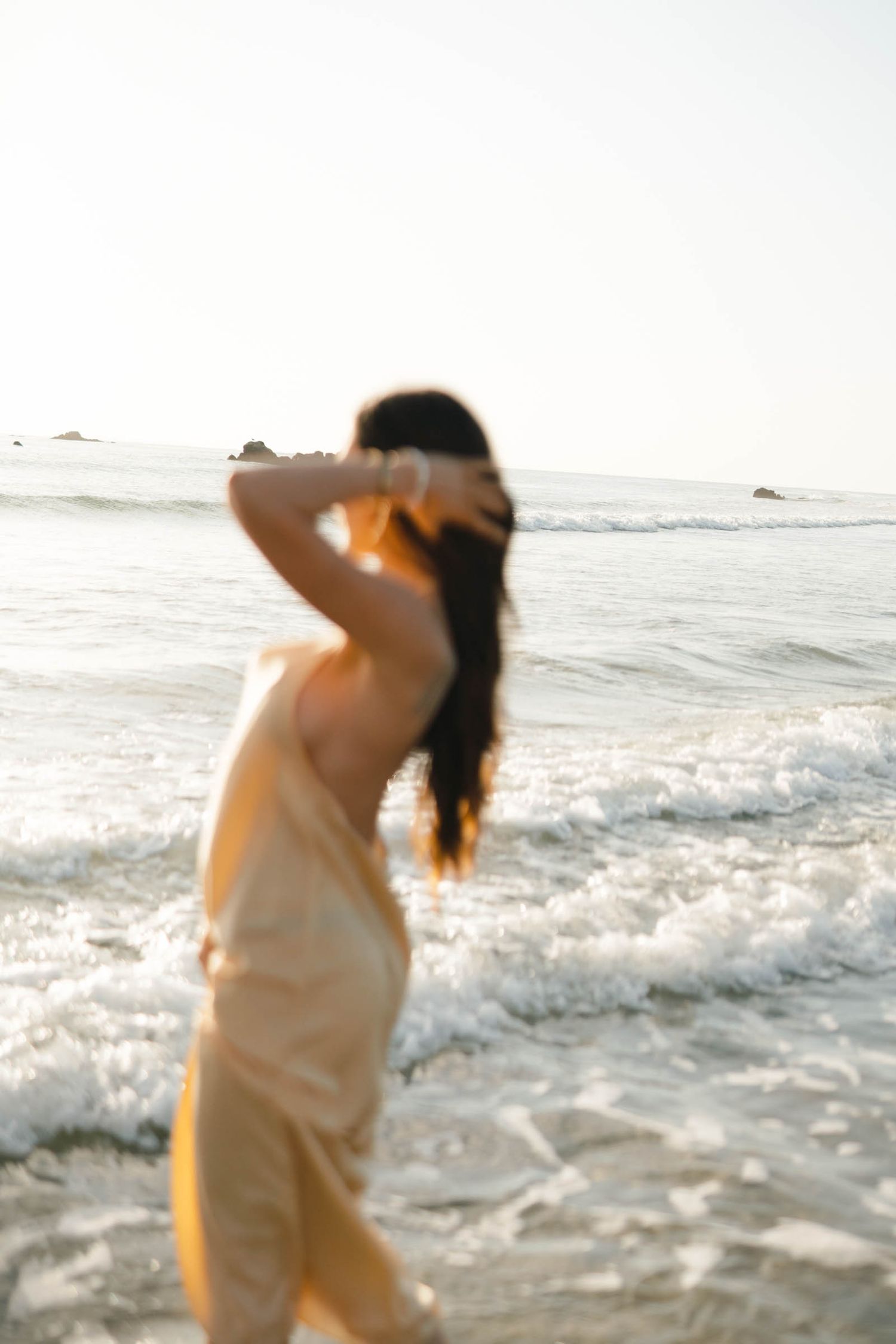 Blurred silhouette of woman in cream dress dancing by ocean waves.
