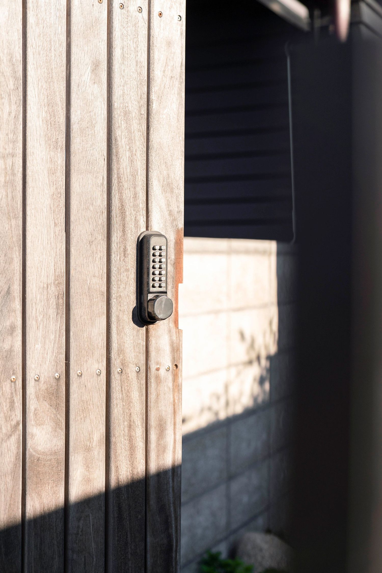 Digital keypad lock mounted on a weathered wooden door casting a dramatic shadow in natural lighting.