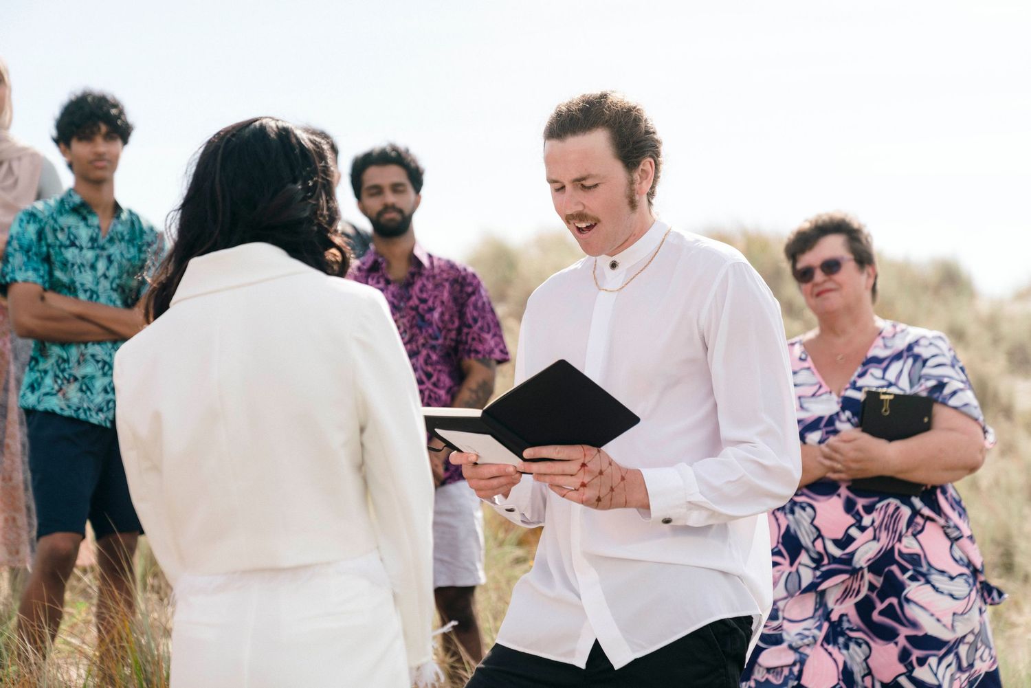 Joyful wedding guests sharing laughs and embraces on a scenic beach overlook.