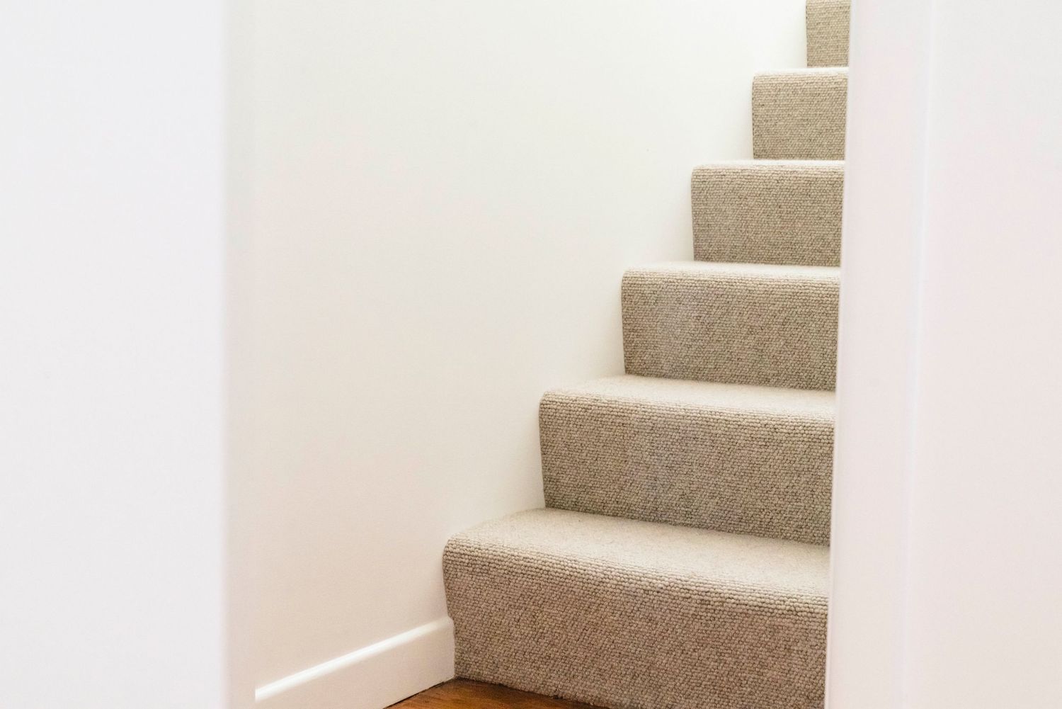 Carpeted staircase with beige runner ascending against white walls in modern home.