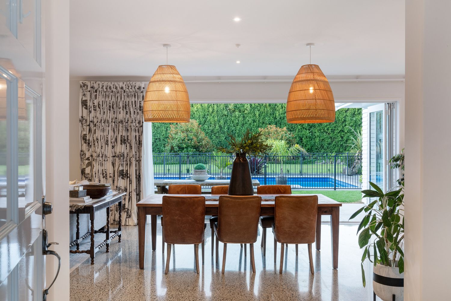 Elegant dining area with woven pendant lights and floor-to-ceiling windows overlooking pool.