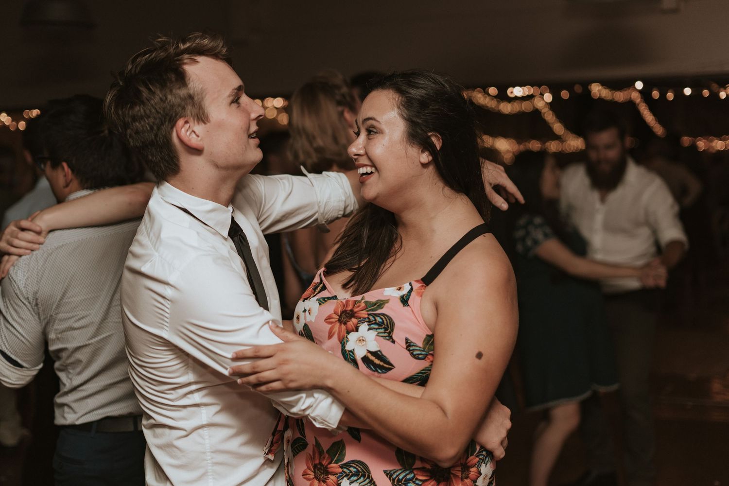 A couple dancing and laughing together at a dimly lit wedding reception.