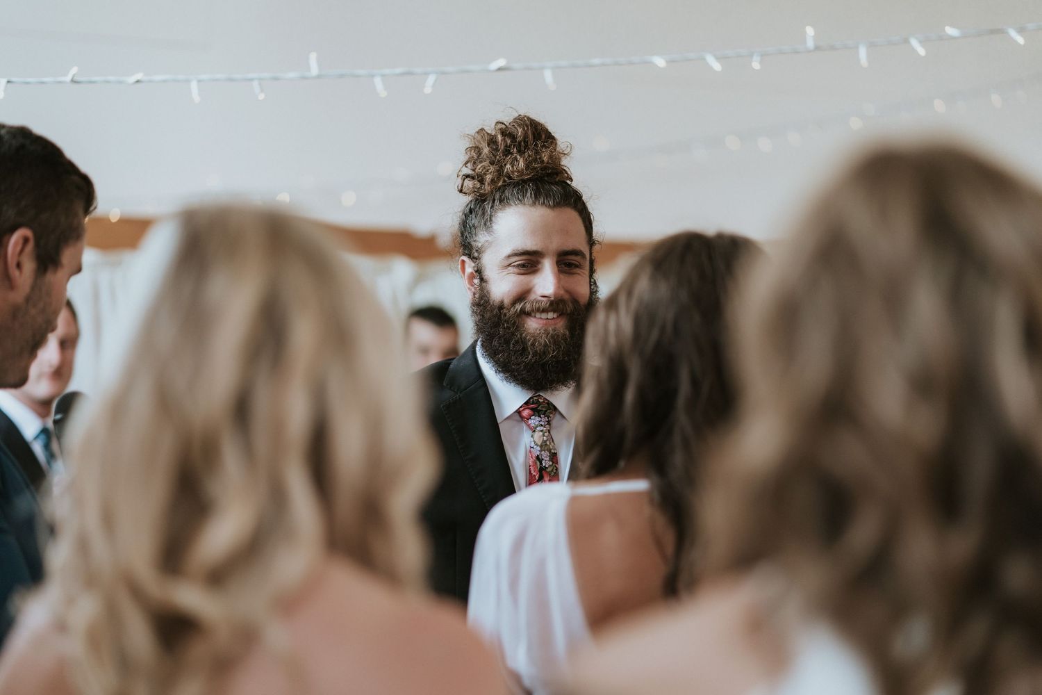 A bearded groom standing with guests during a wedding ceremony with shallow depth of field.