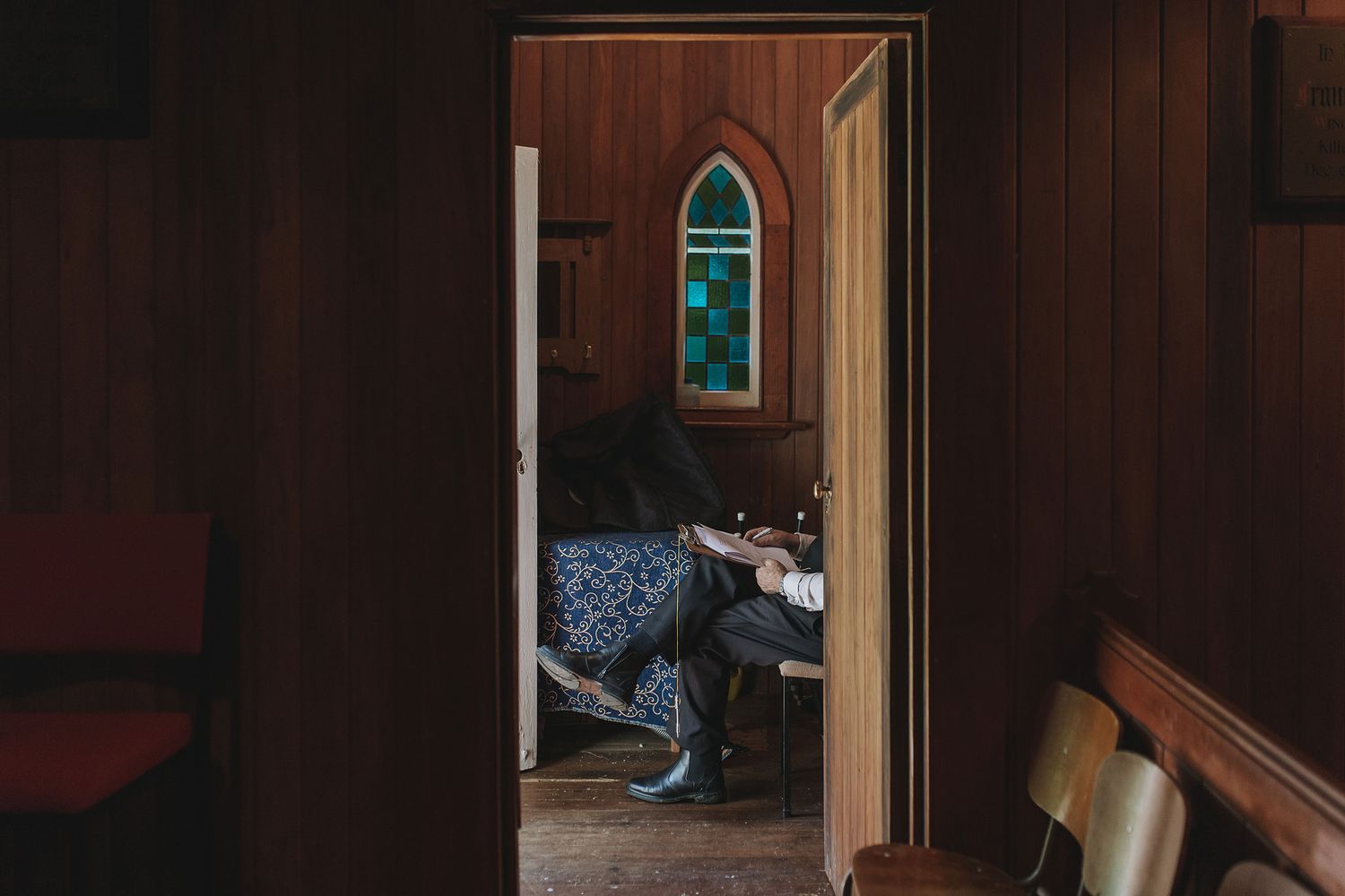 A dog peeks through an open doorway in a church with a stained glass arch window visible.