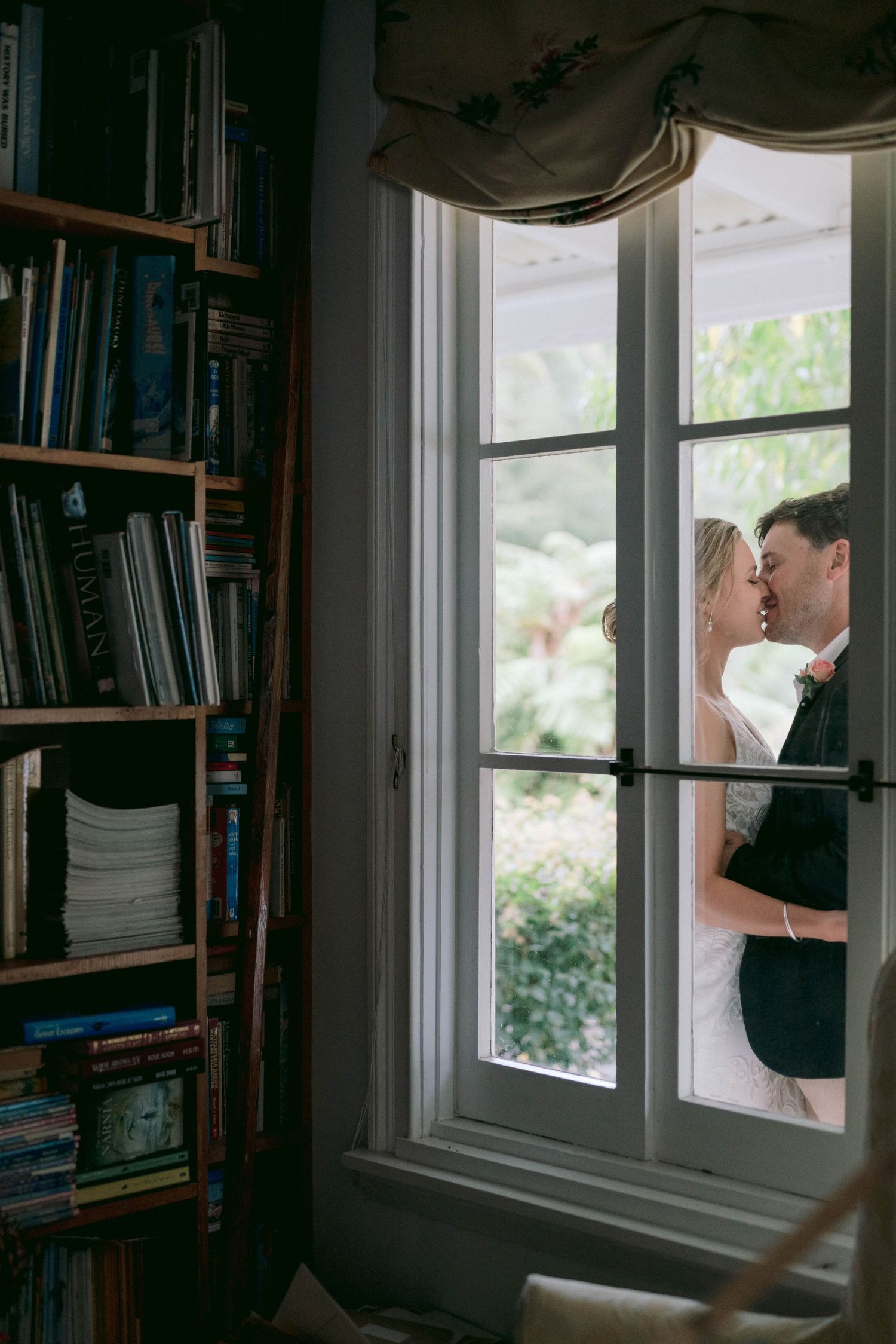 Books line the walls of a cozy window nook with streams of natural light filtering through paned windows.