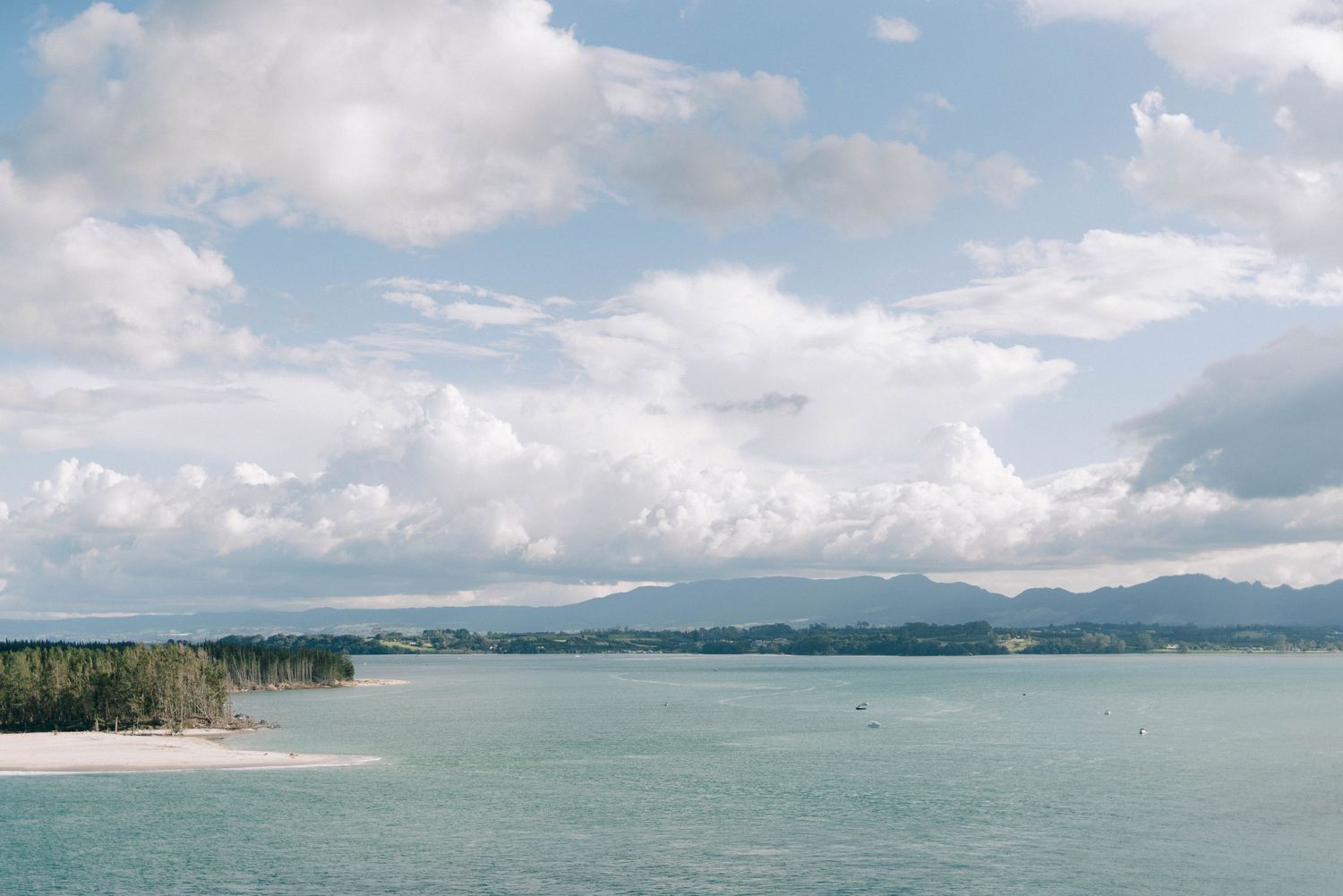 Panoramic coastal view with blue waters and distant mountains under scattered clouds.