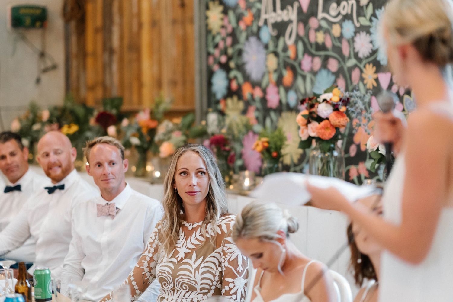 A rustic outdoor wedding reception with long tables set under twinkling lights in a barn or garden setting.